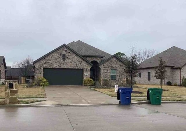 french provincial home with an attached garage, driveway, brick siding, and roof with shingles