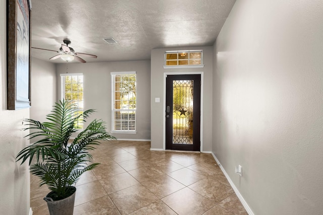 tiled entryway with visible vents, baseboards, a textured ceiling, and ceiling fan