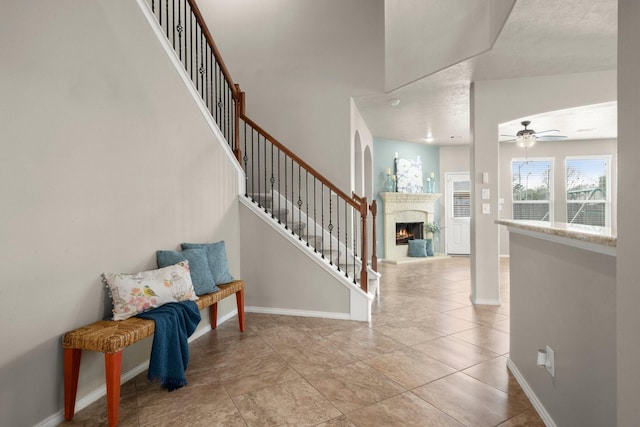 foyer with a ceiling fan, stairs, light tile patterned flooring, a lit fireplace, and baseboards