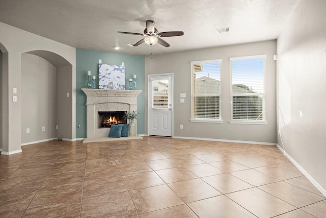 unfurnished living room featuring visible vents, arched walkways, a premium fireplace, a ceiling fan, and tile patterned flooring