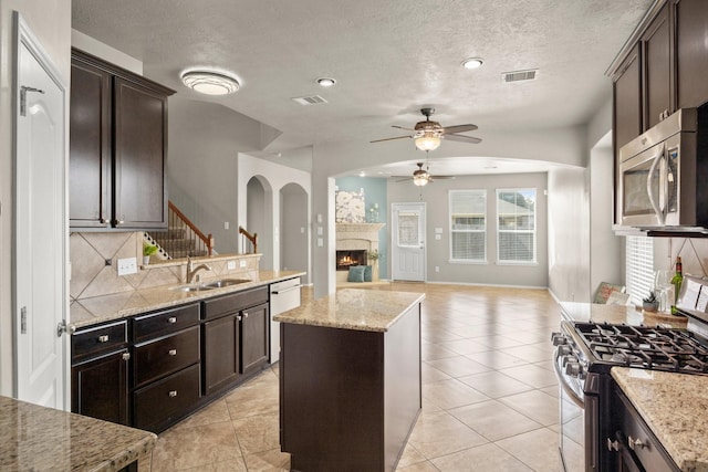 kitchen featuring a sink, a warm lit fireplace, ceiling fan, dark brown cabinetry, and appliances with stainless steel finishes