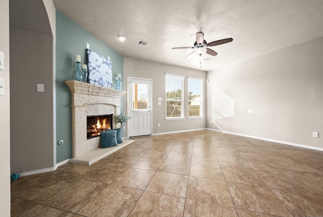 unfurnished living room with a ceiling fan, a textured ceiling, a lit fireplace, baseboards, and visible vents