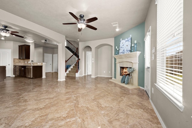 unfurnished living room featuring ceiling fan, a healthy amount of sunlight, and stairs