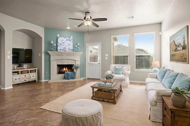 living room featuring tile patterned floors, visible vents, a premium fireplace, baseboards, and ceiling fan