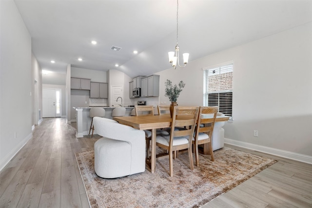 dining room with light wood-type flooring, baseboards, visible vents, a chandelier, and lofted ceiling