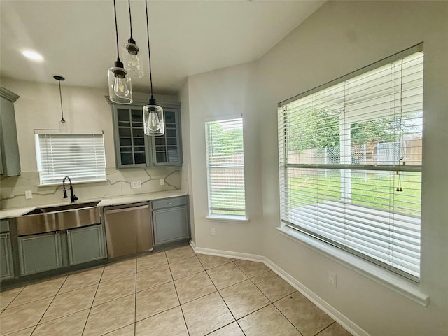 kitchen with stainless steel dishwasher, tasteful backsplash, a sink, light tile patterned floors, and light countertops
