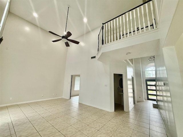 unfurnished living room featuring ceiling fan, baseboards, a towering ceiling, and light tile patterned floors