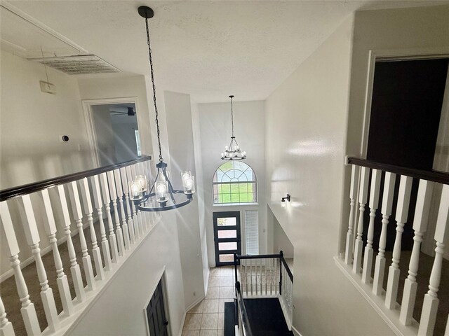 interior space with tile patterned floors, visible vents, baseboards, a towering ceiling, and a notable chandelier