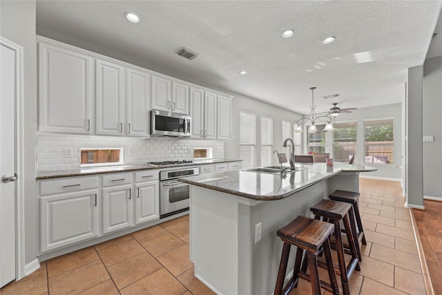 kitchen with a sink, a breakfast bar area, white cabinetry, backsplash, and appliances with stainless steel finishes
