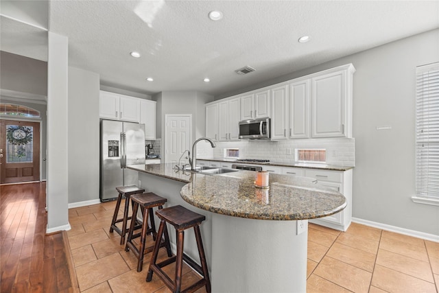 kitchen with a sink, stainless steel appliances, visible vents, backsplash, and baseboards
