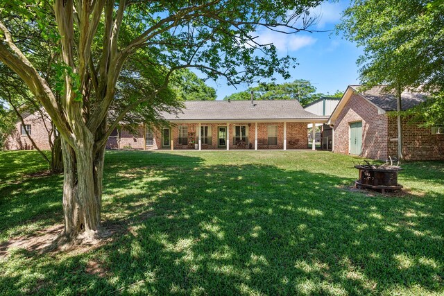 rear view of property with a fire pit, brick siding, and a yard