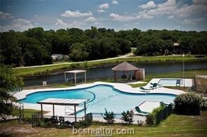 community pool featuring a water view, a patio area, and a wooded view