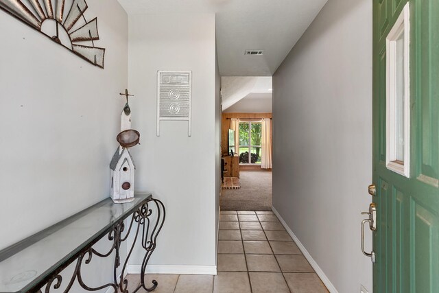 foyer entrance with baseboards, light carpet, visible vents, and light tile patterned floors