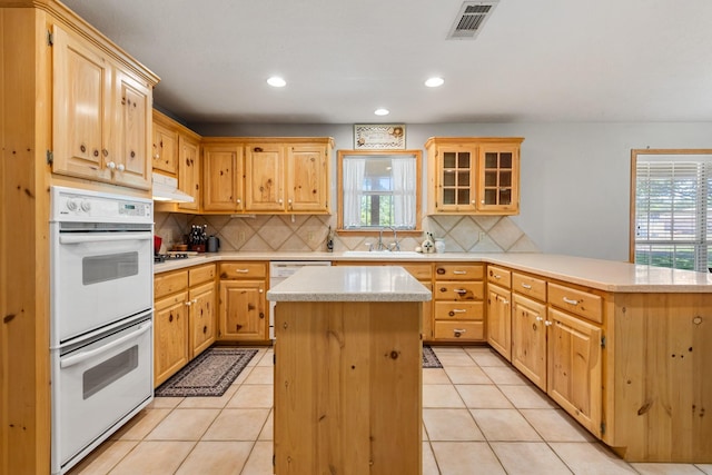 kitchen with light countertops, a sink, white appliances, a kitchen island, and a peninsula