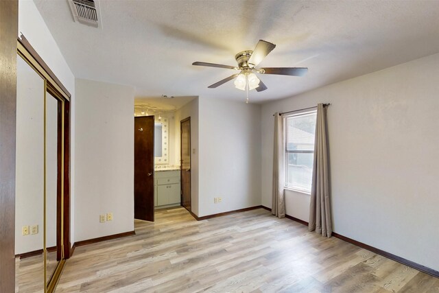 unfurnished bedroom with a closet, connected bathroom, light wood-style flooring, baseboards, and visible vents