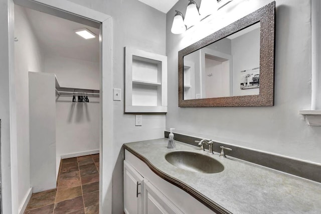 bathroom featuring a walk in closet, stone finish floor, baseboards, and vanity