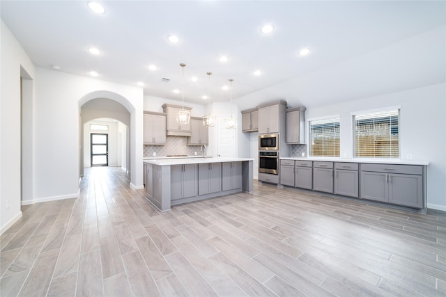 10419 Rigel Ridge Way, Richmond, TX 77406 - kitchen featuring gray cabinetry, stainless steel appliances, arched walkways, light countertops, and backsplash