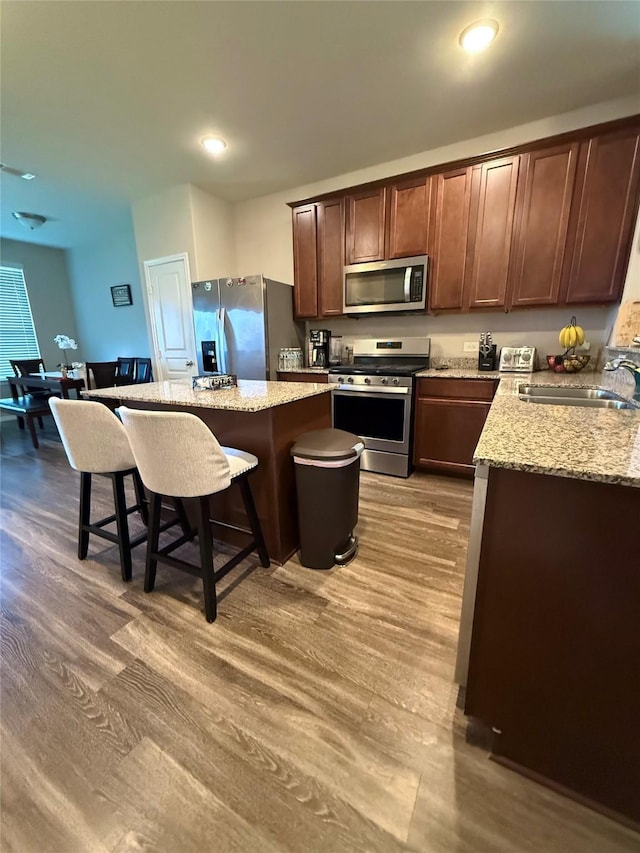 kitchen with a kitchen breakfast bar, wood finished floors, a sink, a center island, and appliances with stainless steel finishes