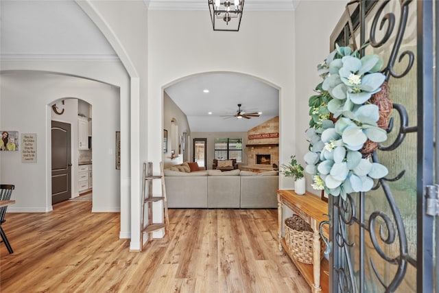 foyer featuring arched walkways, light wood finished floors, ceiling fan, and a large fireplace