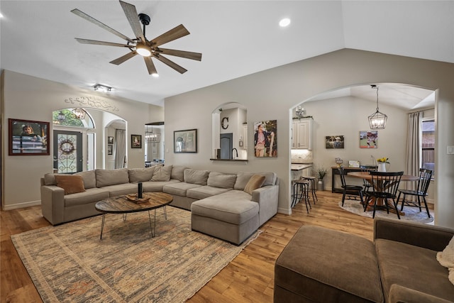 living area with arched walkways, ceiling fan, vaulted ceiling, and light wood-style flooring