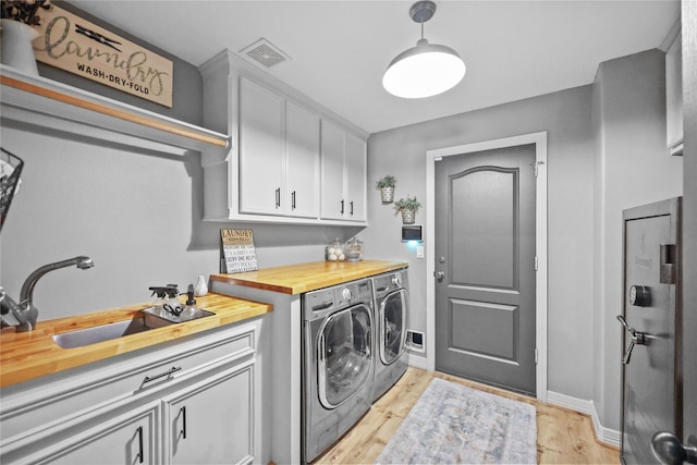 clothes washing area featuring visible vents, light wood-type flooring, cabinet space, a sink, and separate washer and dryer