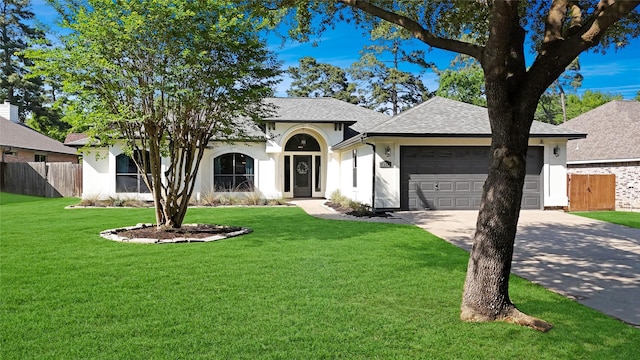 ranch-style home with driveway, a front yard, roof with shingles, fence, and an attached garage