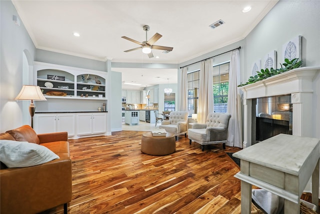 living room with crown molding, ceiling fan, visible vents, and wood finished floors
