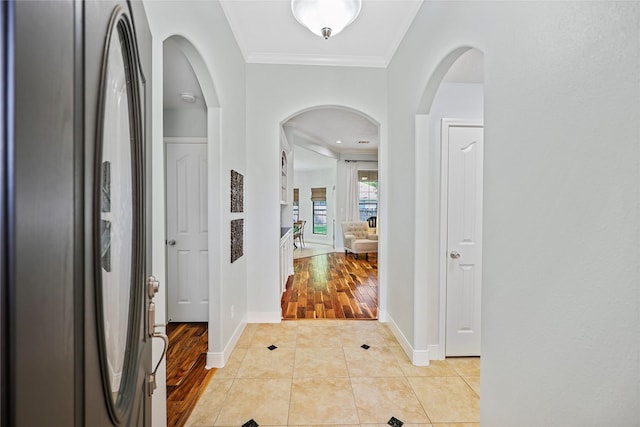 hall with crown molding, light tile patterned flooring, baseboards, and arched walkways