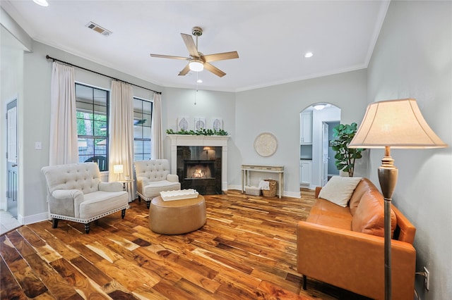 living area with visible vents, ornamental molding, wood finished floors, arched walkways, and a ceiling fan