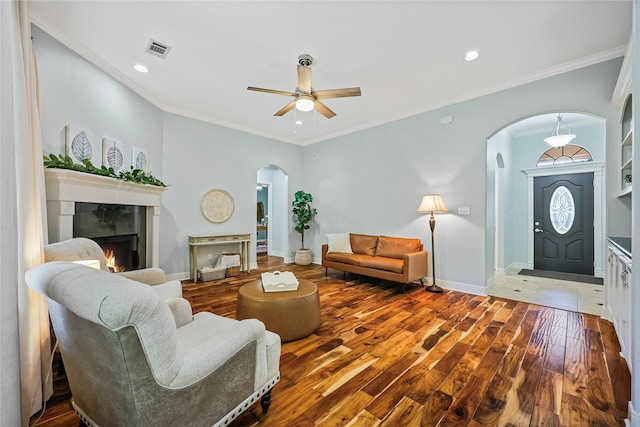 living area with a lit fireplace, a ceiling fan, visible vents, arched walkways, and wood finished floors