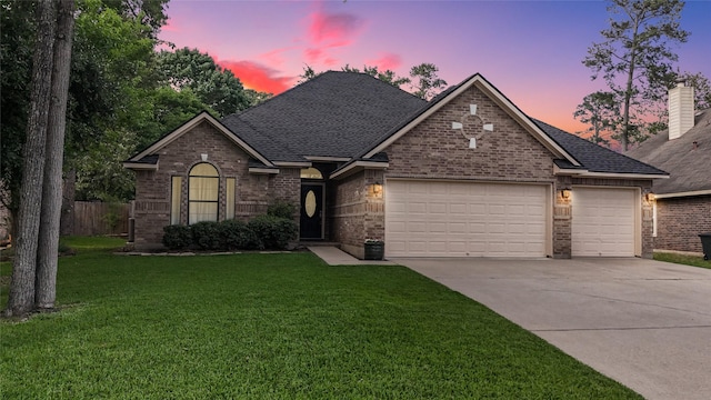 ranch-style home featuring driveway, roof with shingles, a lawn, brick siding, and an attached garage