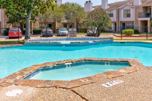 view of swimming pool featuring a pool with connected hot tub and fence