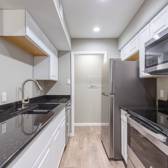 kitchen with dark stone counters, white cabinetry, stainless steel appliances, and a sink