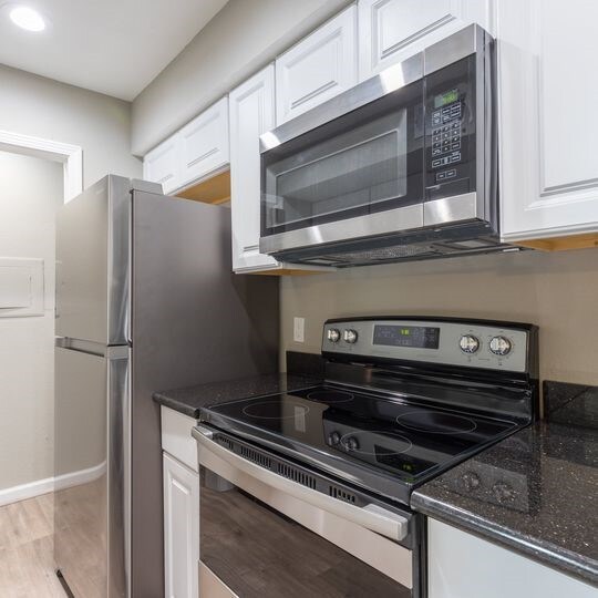 kitchen with dark stone counters, light wood-style floors, white cabinetry, and appliances with stainless steel finishes