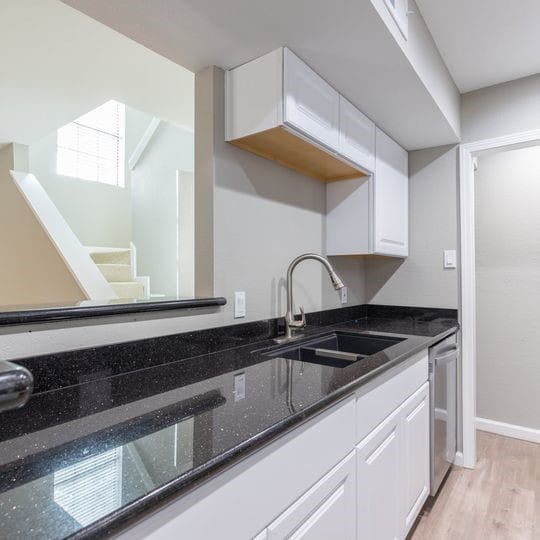 kitchen with white cabinets, stainless steel dishwasher, a sink, dark stone counters, and light wood-style flooring
