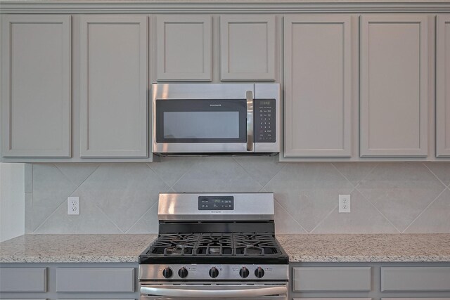kitchen with stainless steel appliances, backsplash, light stone counters, and gray cabinets