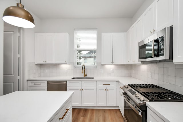 kitchen featuring white cabinets, light wood-style flooring, a sink, light countertops, and appliances with stainless steel finishes