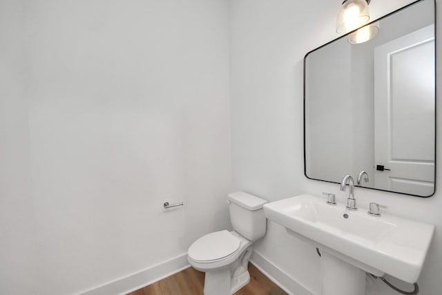bathroom featuring wood finished floors, toilet, baseboards, and a sink