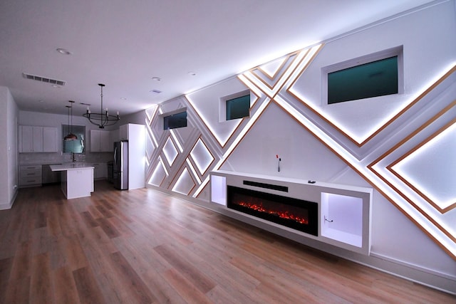 unfurnished living room featuring a glass covered fireplace, wood finished floors, visible vents, and a sink