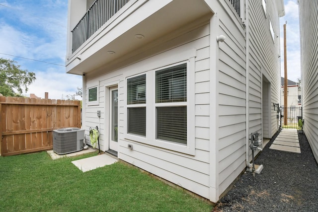 view of property exterior with central AC, fence, a balcony, and a lawn