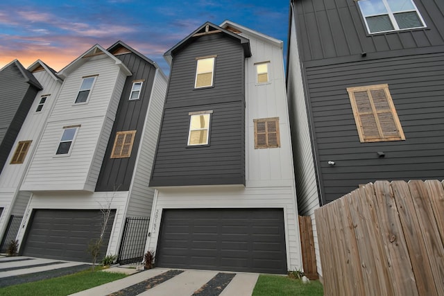 view of front of property featuring board and batten siding, driveway, fence, and a garage