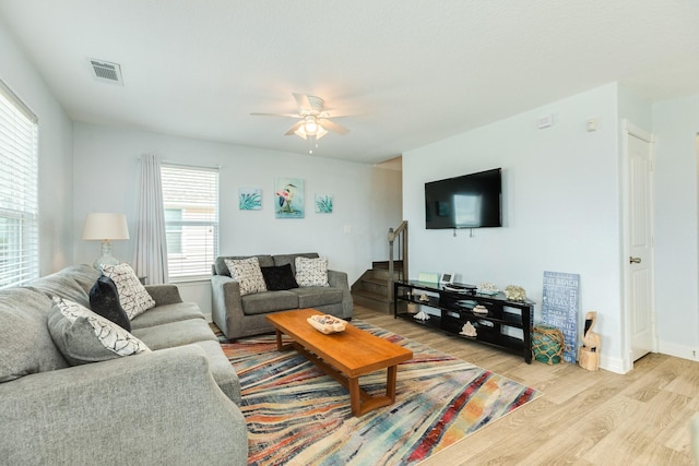 living room featuring visible vents, baseboards, stairway, a ceiling fan, and light wood-style flooring