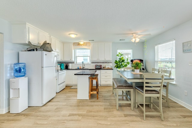 kitchen featuring dark countertops, light wood-type flooring, a sink, white appliances, and white cabinetry