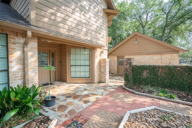 exterior space featuring a patio area, a shingled roof, and brick siding