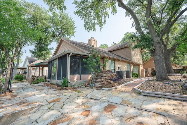 rear view of property featuring a chimney, fence, central air condition unit, a patio, and a sunroom