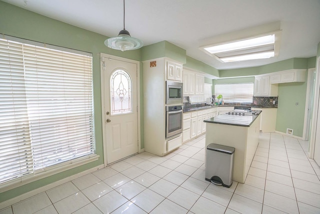 kitchen with white cabinets, stainless steel appliances, a center island, tasteful backsplash, and light tile patterned floors