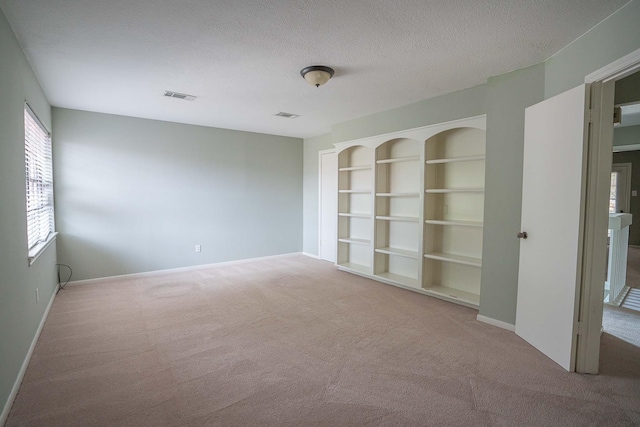 unfurnished room with baseboards, carpet, visible vents, and built in shelves