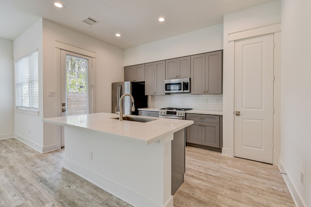 2718 Oakwood Crest Ln, Houston, TX 77018 - kitchen featuring gray cabinets, a sink, light wood-style floors, a center island with sink, and appliances with stainless steel finishes
