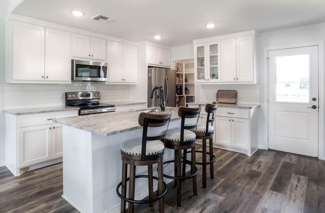 418 E St, East Bernard, TX 77435 - kitchen with stainless steel appliances, visible vents, glass insert cabinets, a breakfast bar area, and white cabinetry