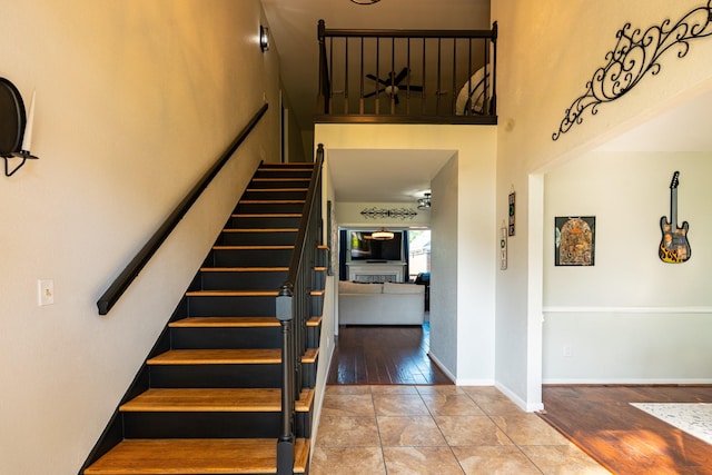 stairs with wood finished floors, a high ceiling, and baseboards